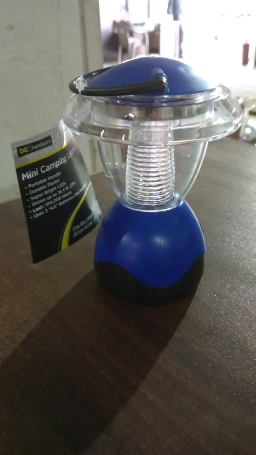 A blue and clear plastic mini lantern with a black handle and a product tag hangs on a dark brown surface.