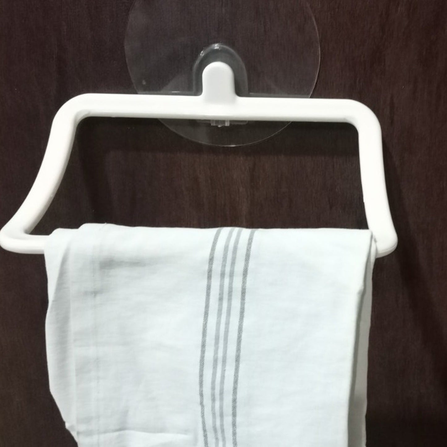 A sleek self-adhesive towel holder mounted on a tiled bathroom wall, holding a white hand towel.